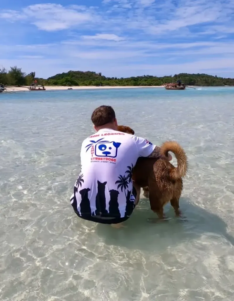 Vrijwilliger van Samui Street Dogs in zee met een geredde hond